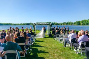 Outdoor lakeside wedding ceremony setup with white chairs and floral arch against a scenic water backdrop.
