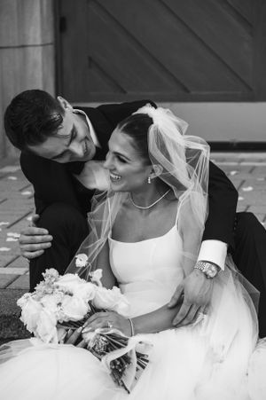 A black and white portrait of newlyweds sharing an intimate moment while sitting with a bouquet of flowers.
