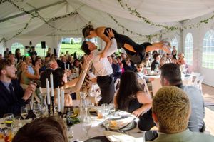 Wedding guests perform dramatic lift during reception celebration under white tent.