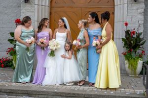 Bridesmaids in pastel dresses of varying colors gather with the bride outside a church entrance.