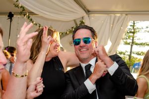 Wedding reception guests dancing and celebrating with sunglasses and raised hands.