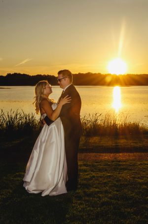 A romantic sunset photoshoot by a lake with a couple embracing in formal attire.