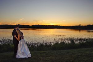 A couple stands together against a sunset backdrop overlooking a serene lake.