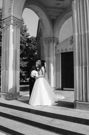 Black and white wedding photo of couple in elegant archway with ornate architectural details.