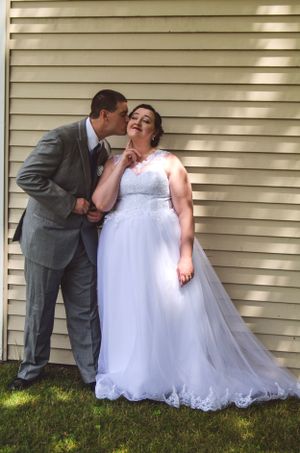 A romantic moment between newlyweds in formal attire against white siding on their wedding day.