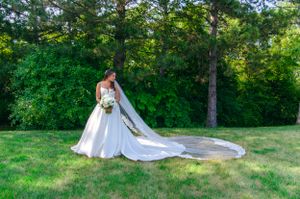 Bride in flowing white gown walking in a lush green garden setting with long train trailing behind.