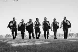 Black and white photo of groomsmen jumping in unison on a grassy hill.