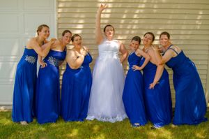 Wedding party in royal blue bridesmaid dresses posing playfully on grass.