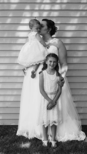 Wedding portrait with children in white dresses against siding background.