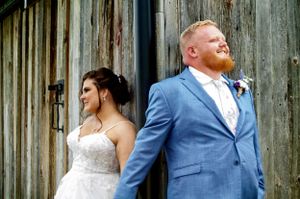 Wedding couple poses against rustic wooden barn door in formal attire.