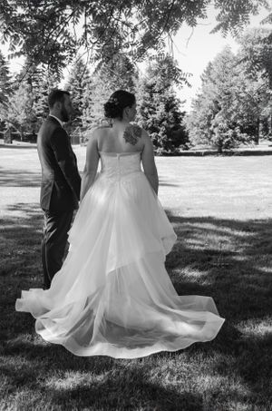 Newlywed couple standing on lush grass with flowing white wedding dress in black and white photography.