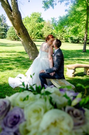 Romantic wedding couple sharing intimate moment under tree with bouquet in foreground.