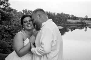 Joyful couple sharing tender moment by lakeside in black and white wedding photo.