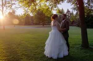 Couple in wedding attire embraces during golden hour in park setting.