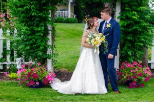 Newlyweds pose in a beautiful garden setting surrounded by pink flowers and greenery.