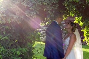 Romantic wedding couple shares a moment in dappled sunlight under green trees.