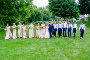 Wedding party lined up on green lawn wearing pink dresses and navy suits.