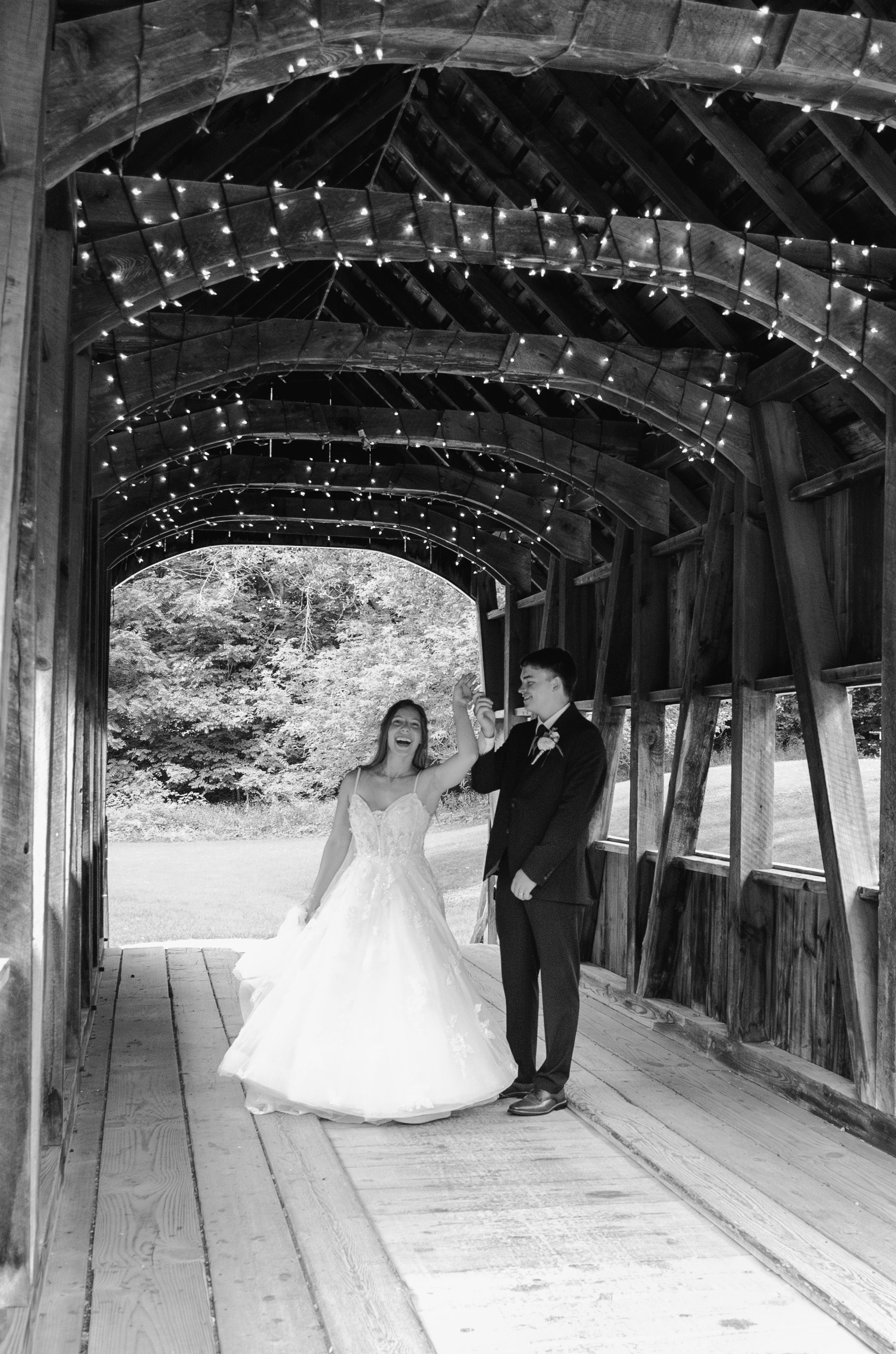 Couple poses inside covered bridge decorated with twinkling fairy lights.