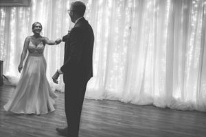 Black and white photo of couple dancing in elegant reception venue with sheer curtain backdrop.