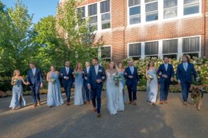 Wedding party in blue and navy attire walking together outside brick building.