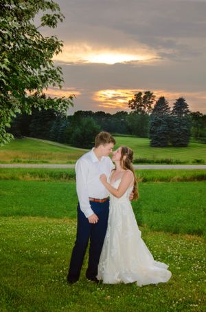 Newlyweds embrace during golden sunset on a lush golf course with evergreen trees in background.