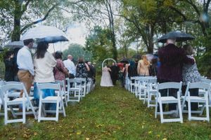 Wedding ceremony setup with white chairs on rainy day with guests holding umbrellas.