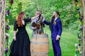 Outdoor ceremony setup with floral arch and wooden barrel in a green garden setting.