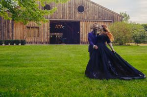A dramatic wedding shoot in front of a rustic wooden barn with a couple wearing elegant black attire on lush grass.