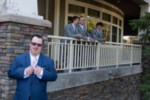 Groomsmen in suits stand on stone porch during wedding preparations.