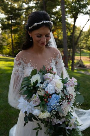 Beautiful wedding bouquet featuring white, blue and pink flowers with delicate greenery in an outdoor garden setting.