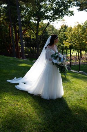 Elegant white wedding gown with flowing train photographed on a sunlit grassy hillside.