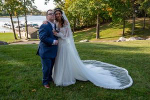 Romantic wedding photo on green lawn with lake and autumn trees in background.