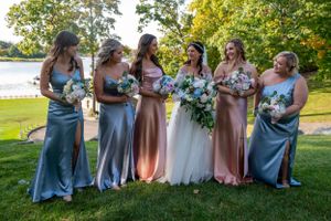 Wedding party in pastel blue and pink dresses poses by lakeside with bouquets.