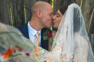 A bride and groom share a romantic kiss outdoors with delicate strings of lights in the background.