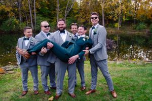 Groomsmen in grey suits playfully posing outdoors during wedding festivities.