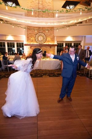 Couple dancing at wedding reception venue decorated with string lights and greenery.
