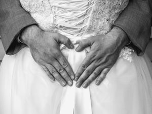 Black and white detail shot of hands resting on white fabric with lace details.
