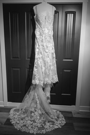 Elegant lace wedding dress with floral appliques and cathedral train hanging on dark double doors, black and white photo.