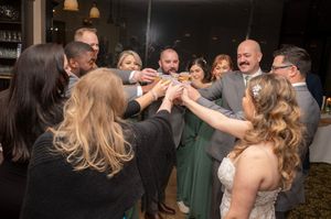 Wedding guests dancing together in celebration at an indoor reception venue with dim lighting and festive atmosphere.
