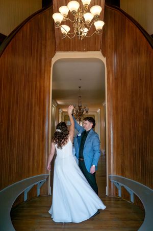 Bride and groom dancing in an elegant wood-paneled hallway with chandelier lighting during their wedding reception.