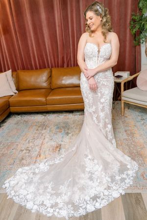 A bride in a fitted lace wedding gown with sweetheart neckline poses showing the dramatic train and floral details.