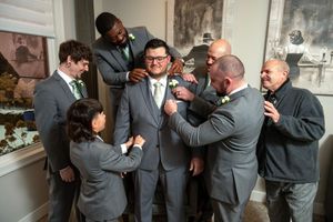 Groomsmen in gray suits help adjust the groom's tie and attire while getting ready before the wedding ceremony.
