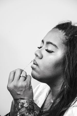 Black and white portrait of a young woman applying lip gloss, wearing a floral jacket and ring.