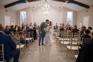 A bright white wedding chapel interior with crystal chandeliers and gold chiavari chairs arranged in rows for a ceremony.
