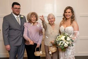 A group of four people pose together at a wedding celebration, with the bride holding a white floral bouquet.