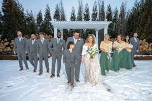 Wedding party wearing grey suits and green dresses poses together in snowy winter landscape for outdoor photos.