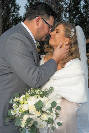 A romantic wedding couple shares an intimate kiss while the bride holds a beautiful bouquet of white roses and greenery.