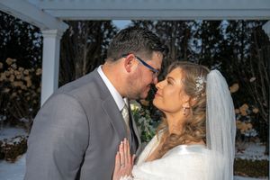 A romantic wedding couple shares a tender kiss on their special day in front of a white pillar backdrop.