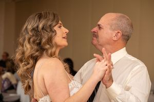 A couple shares a joyful dance together at a formal event, laughing and embracing in a series of candid moments.