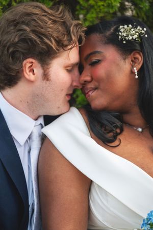 Interracial couple in wedding attire sharing a romantic moment, bride wearing white gown with floral hair accessory.